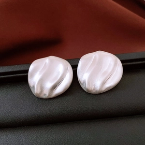 Detail of silver wavy earrings with brushed metal texture on a textured leather display
