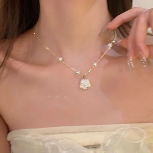 Nahaufnahme der eleganten Goldblumendose und Perlenkette am Hals des Models
