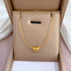 Dettaglio macro della collana a serpente dorata con pendente cilindrico curvo minimalista