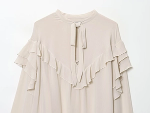 Detail of beige long sleeve blouse featuring tiered ruffles and elegant neckline tie
