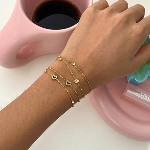 Detailed view of layered 18k gold-plated bracelets featuring heart and cubic zirconia charms