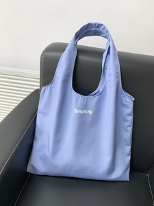Detail of lavender canvas tote with white Simplicity text on a black leather couch