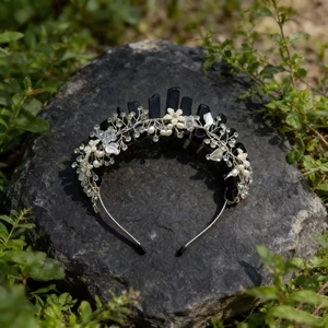 Detailed shot of handmade rose quartz crown with white flowers and crystals on a rock