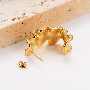 Polished 18k gold irregular wave stud earrings on a beige travertine stone display
