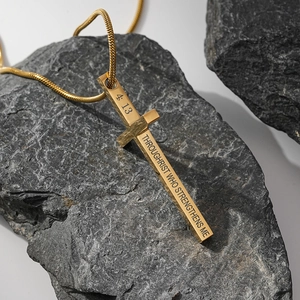 Collier croix en acier inoxydable doré avec gravure religieuse sur un fond en pierre sombre