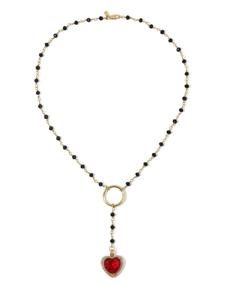Detail of gold chain necklace with black beads and a red heart pendant with zircons