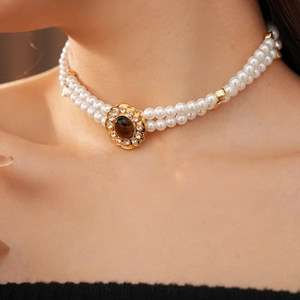 Dettaglio collana di perle a due fili con ciondolo a fiore dorato e occhio di tigre