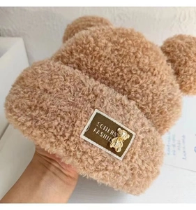 Detail of warm brown plush teddy hat showing fuzzy texture and golden bear ornament