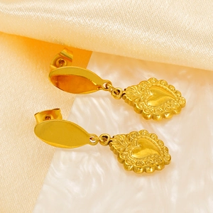 Détail de boucles d'oreilles cœur dorées avec motif en relief sur tissu brillant