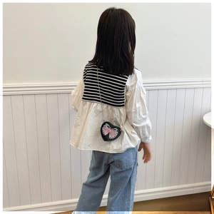 Detail of a black heart-shaped crossbody bag with butterfly applique on a girls outfit