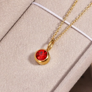 Macro shot of gold necklace featuring a polished round red birthstone pendant on velvet