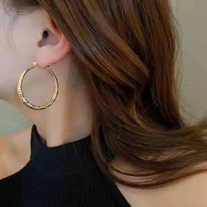 Close-up of golden textured hoop earrings with a hammered surface on a female model