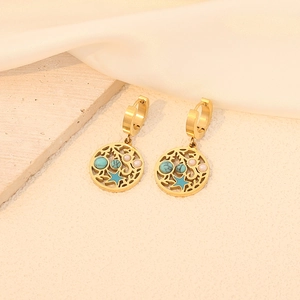 Detailed shot of golden hollow earrings with turquoise and pearl on a textured surface