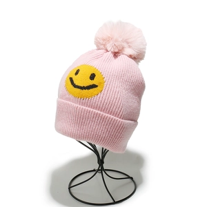Pink chunky knit beanie with large fur pom-pom and yellow smiley face patch for women