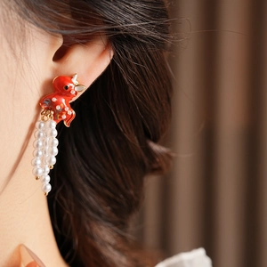 Close-up of vintage red goldfish earrings with elegant white pearl tassels on a model