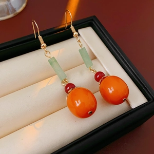 Detail of persimmon drop earrings with green and orange beads on a jewelry cushion