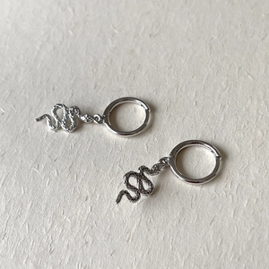 Macro shot of silver snake drop earrings with textured scales on beige art paper