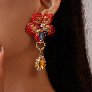 Détail de boucle d'oreille fleur brodée rouge avec goutte ambrée et cœur en cristal