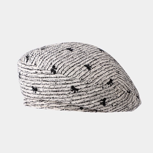 Detail of tweed beret featuring black bow patterns and refined woven texture for women