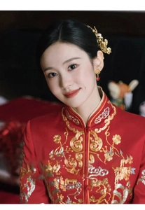 Close-up of golden hollow flower earring with red bead on traditional red bridal embroidery