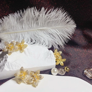 Elegant gold flower earrings and ring set with sparkling crystals on a textured background