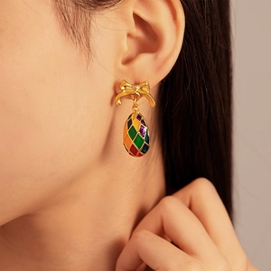 Close-up of vintage golden bow earrings with colorful enamel diamond pattern on model