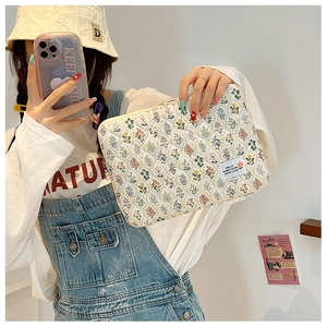 Close-up of beige floral quilted laptop sleeve with HELLO label and zipper detail