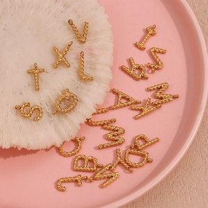 Macro detail of 18K gold plated twisted rope texture letter pendants on coral stone