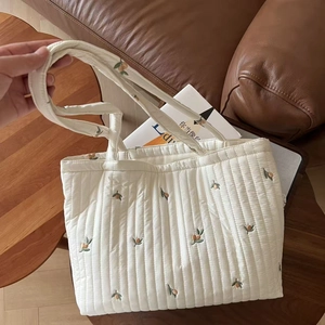 White quilted tote bag with orange fruit embroidery on a cozy living room background
