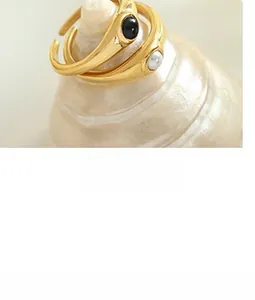 Detail of adjustable gold-plated bar rings featuring black gem and white pearl on a seashell