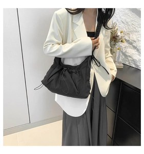 Detailed view of black pleated drawstring tote bag worn over the shoulder by a model