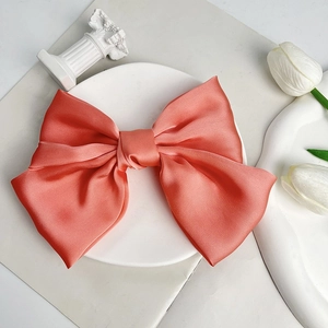Detail of a large peach satin bow hair clip with glossy texture and layered design