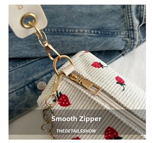 Detailed macro view of gold zipper and metal clip on a white strawberry corduroy bag