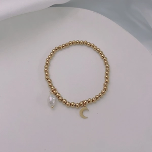 Close-up of gold beaded stretch bracelet with baroque pearl and crescent moon charms