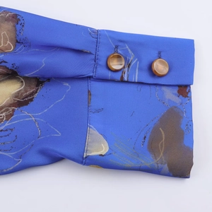Dettaglio del polsino della camicia in raso blu floreale con bottoni in resina marrone