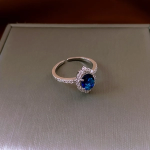 Dettaglio macro di anello con pietra blu ovale e piccoli zirconi su fascia argentata