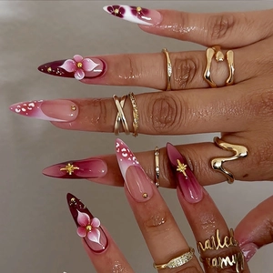 Long stiletto press-on nails with red gradient, 3D floral accents, and gold nail charms
