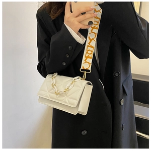 White quilted crossbody bag with gold chain and patterned wide strap shown on black coat