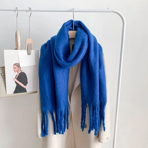 Thick blue cashmere-feel winter scarf with long tassels draped on a beige coat