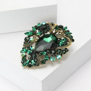 Detailed macro view of vintage gold brooch with pear-cut green gem and crystal inlay