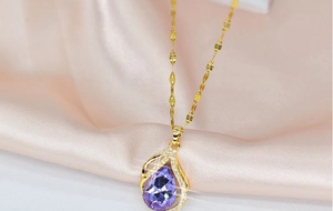 Detail of a gold teardrop necklace with a purple gemstone and small accent stones