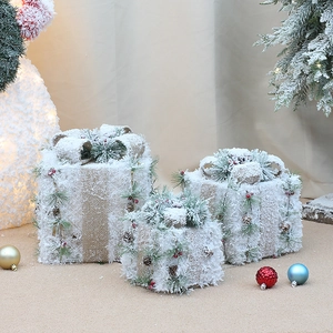 Detailed close-up of three snow-covered gift boxes with pine cones and red berry accents