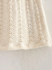 Dettaglio macro della gonna in maglia traforata color crema con motivi a onde