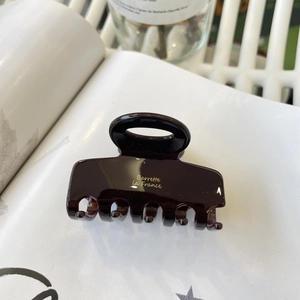 Brown tortoiseshell acetate hair claw clip with golden lettering on a magazine page