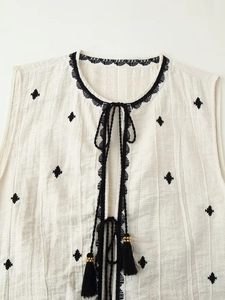 Detail of v-neck embroidered vest with black diamond patterns and tassel ties