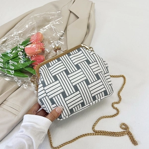 Detail of hand-held shell bag with woven texture and gold chain in a lifestyle setting