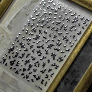 Detail of silver liquid metal nail stickers with irregular 3D droplets in a vintage frame