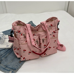 Pink nylon tote bag with red cherry print and multiple zipper pockets on white cloth
