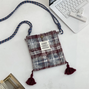 Detail view of red plaid crossbody bag with tassel and rope strap on white desk