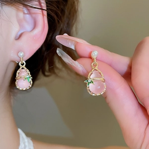 Close-up of pink gourd earrings with pearl and gold leaf detail on a model's ear